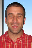 Photo headshot of middle aged white man, short cropped hair, red button down shirt with white plaid.