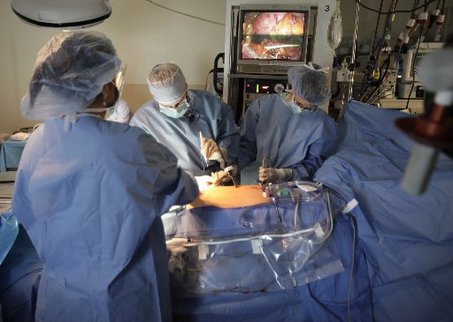 Photo: operating room, three health care providers operating on patient using the aid of a camera.
